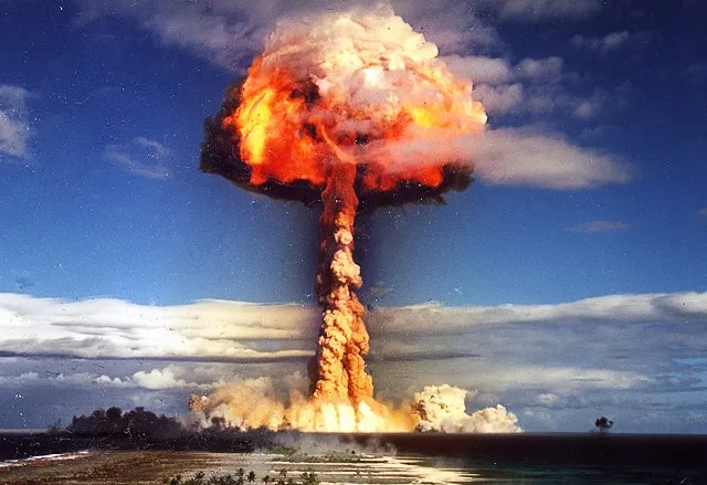 Explozia unei bombe atomice, cu ciuperca de foc și fum ridicându-se deasupra orizontului