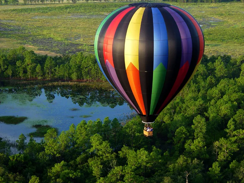 Balon cu aer cald, în dungi colorate, plutind deasupra unei păduri